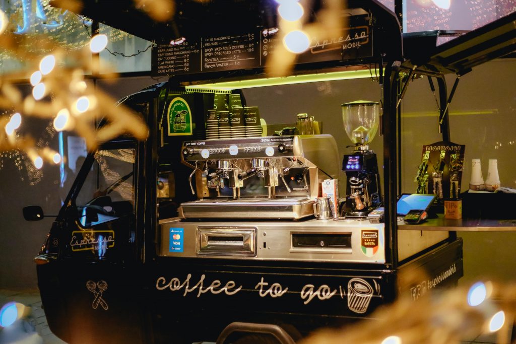 Les coulisses de notre foodtruck : un concept gourmand et fleuri Cozy mobile coffee shop illuminated at night offering coffee to go, wrapped in festive lights.