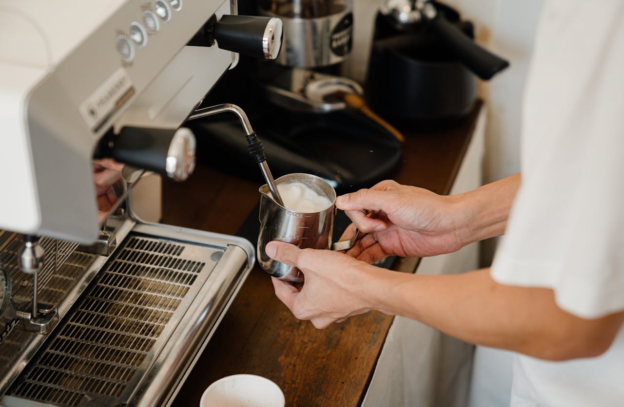 A barista frothing milk with an espresso machine, focusing on the hands and equipment.