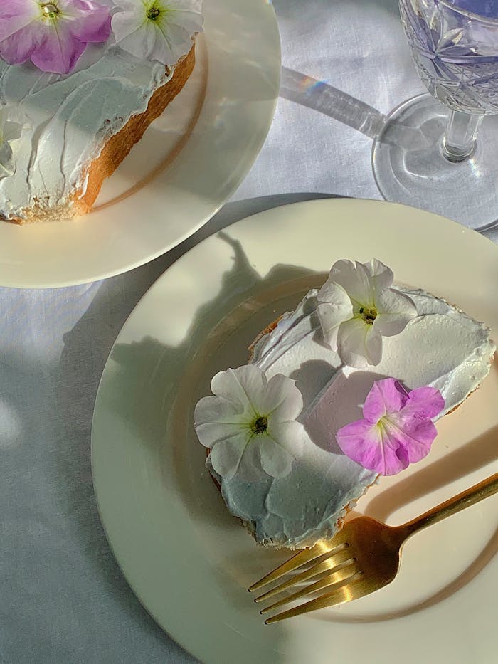A slice of cake with creamy frosting and flowers on a ceramic plate, showcasing elegant food photography.