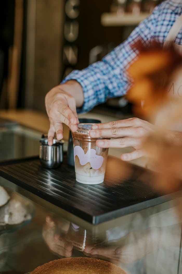 Les coulisses de notre foodtruck : un concept gourmand et fleuri Barista placing lid on iced coffee in café. Hands and beverage close-up.