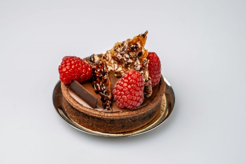 Artisanal chocolate tartlet with raspberries and caramelized nuts on a white background.