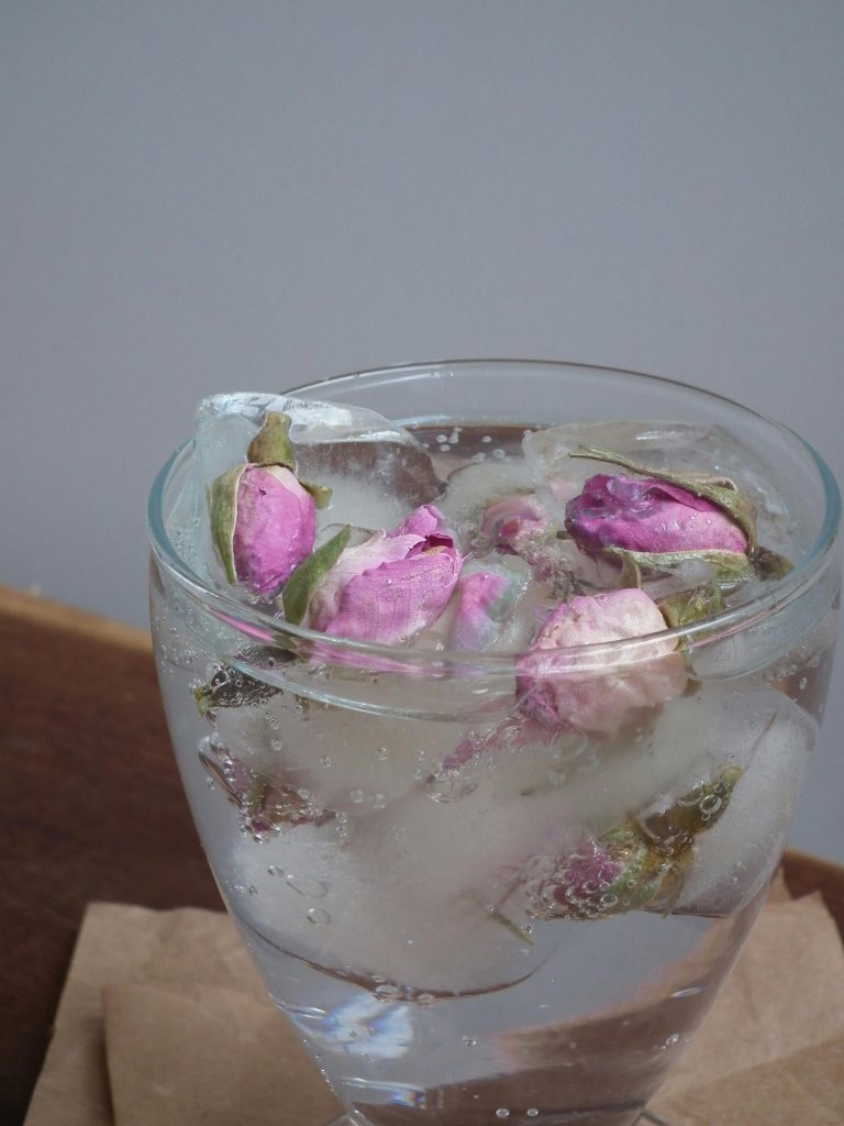 Close-up of purple rose buds in a clear glass with ice.