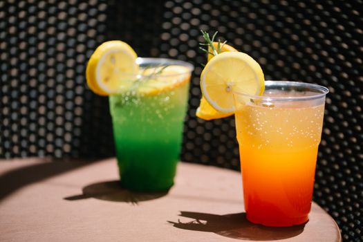 Vibrant lemon drinks in plastic cups with green and orange colors, on a sunny day.